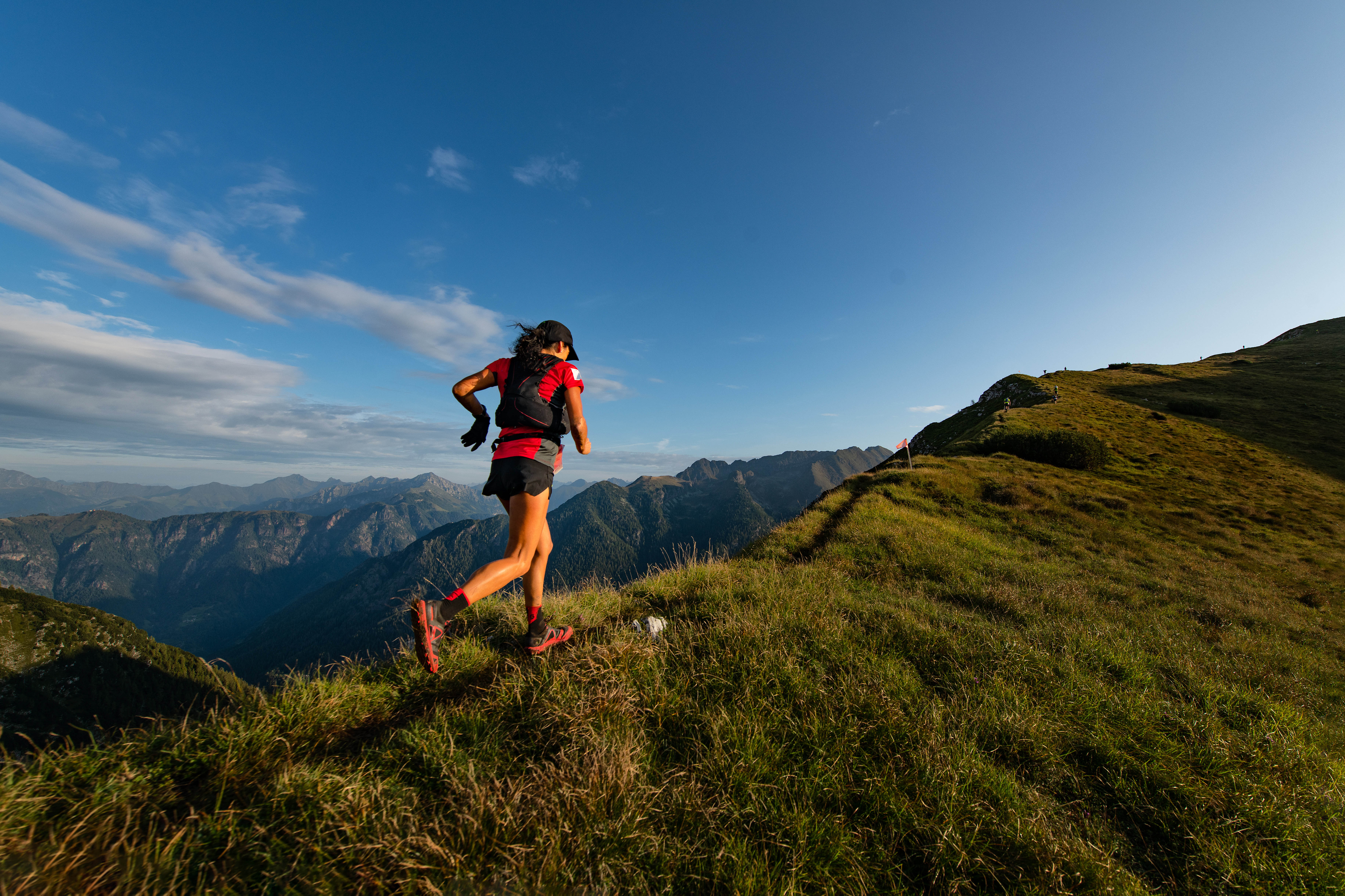 Young fit woman running outside on a mountain, with a bright blue sky in the background